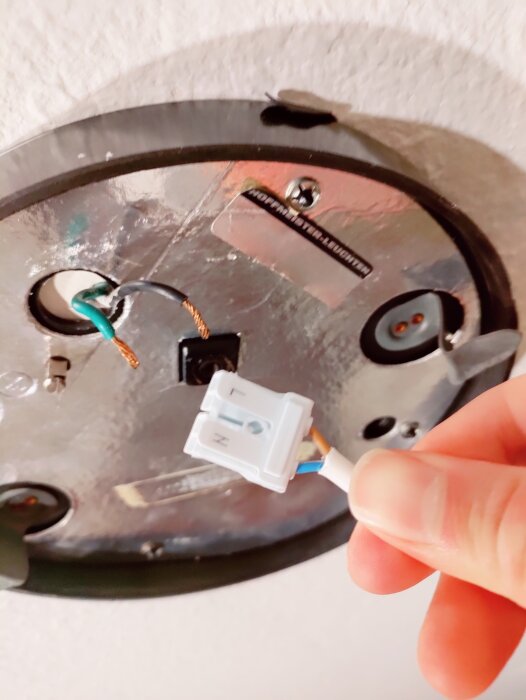 Hand kopplar en elektrisk kontakt till en takarmatur. Kablar synliga, installation, hemreparation, oskarp bakgrund.