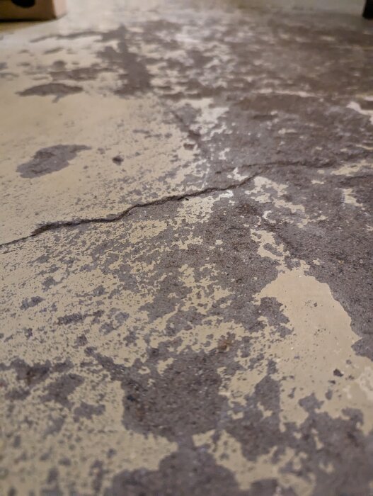 Närbild på slitet betonggolv med flagnande färg och synlig sprickbildning. Nedslitet textur och gråaktiga toner.
