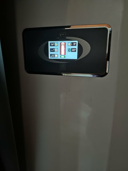 Digital termostatpanel med temperaturinställningar och statusikoner på en vägg.
