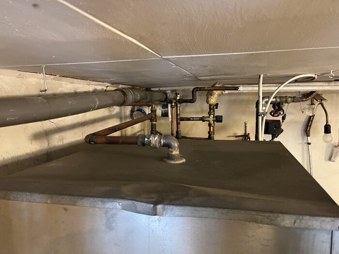 Rörledningar, ventiler och isolering under en betongtak i ett tekniskt utrymme.