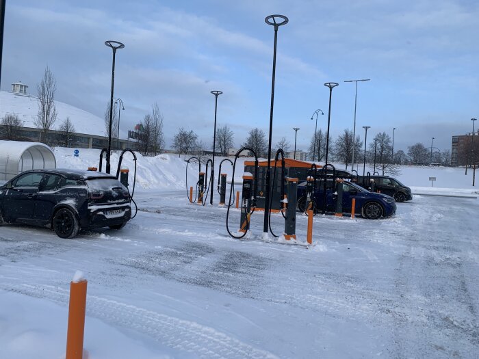 Elbilar laddas vid laddstationer med snötäckt mark och gatlyktor, vinterdag.