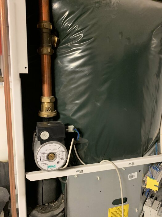 VVS-installation med kopparledningar, cirkulationspump, elanslutningar och en del av en värmepanna eller beredare.
