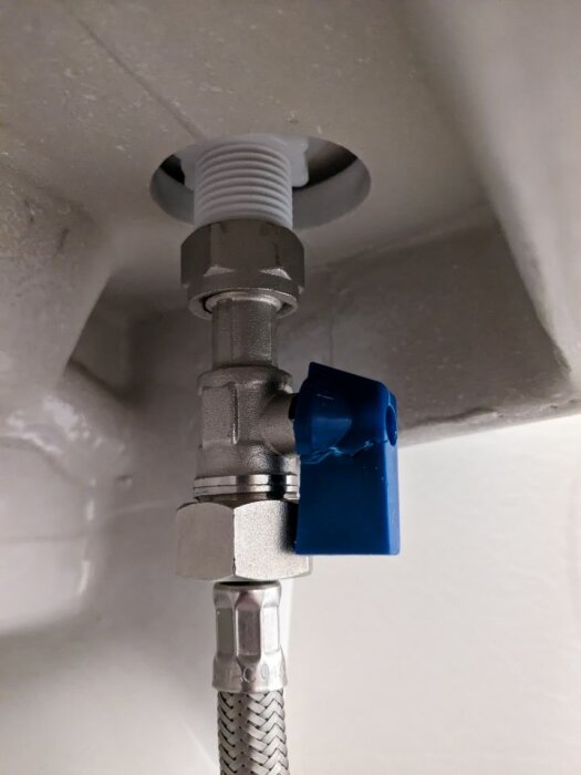 Vattenförsörjningsventil med ansluten flexibel slang och en blå tejpmarkerad spak under vitmålat tak.