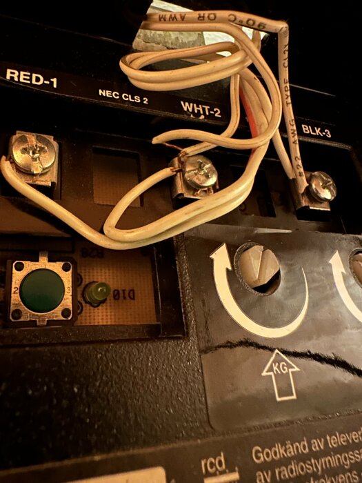Elektrisk komponent med kablar, skruvanslutningar och knappar. Etiketter som RED, WHT, BLK. Teknisk, detaljerat, inre mekanik.