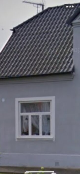 En del av ett hus med takpannor, antenn och ett fönster. Bilden är suddig och beskuren.