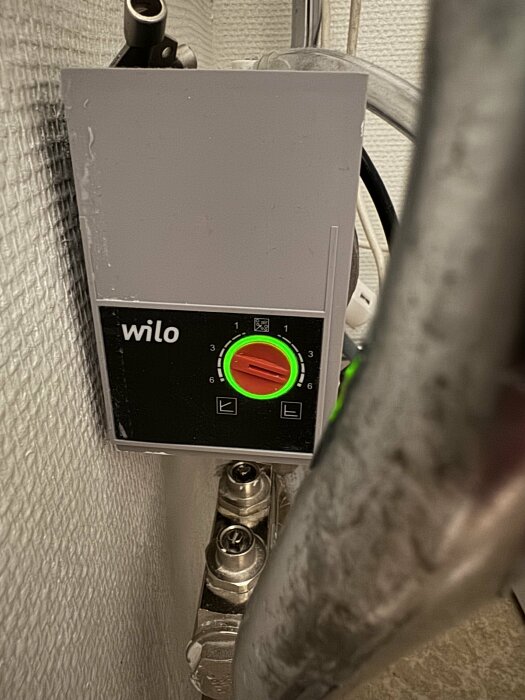 En grå cirkulationspump av märket Wilo med grön lysande skärm, monterad på rörsystem.