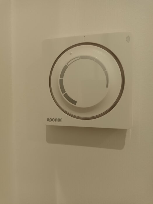 Vit termostat på vägg, inställningshjul, märkt "Uponor", enkelt, modernt, värme styrning.