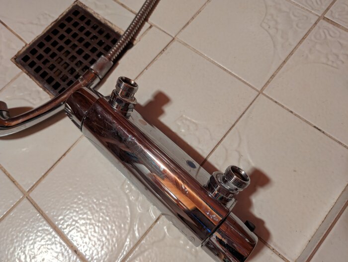 Krom duschblandare på ett kaklat golv, närbild, badrum, skugga, vattenläckage, installation eller reparation.