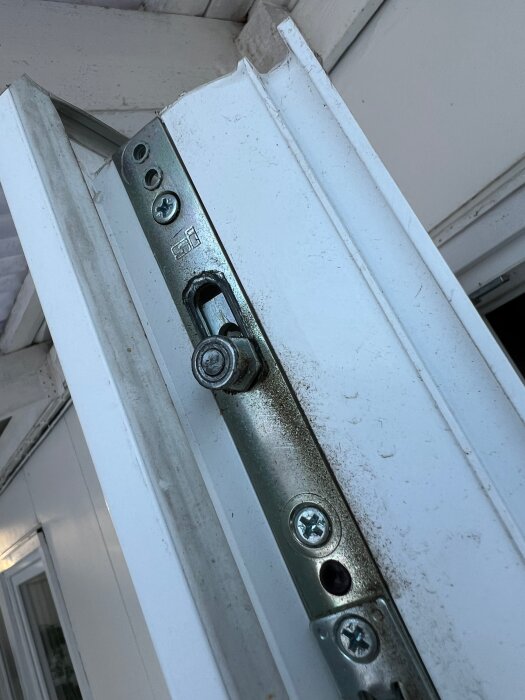 Metallisk dörrstängare monterad på en smutsig vit dörr, synlig mekanism, inga människor, närbild, vinklad översiktsvy.