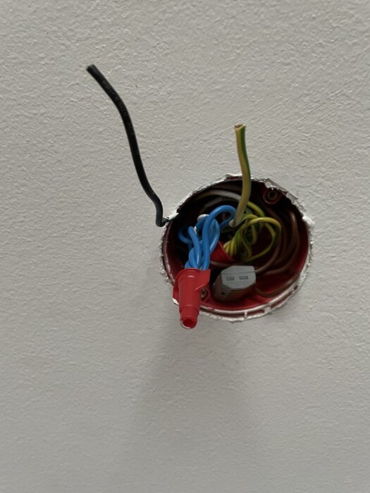 Öppen eldosa i vägg med oskyddade, ej anslutna kablar och en sockel. Installationsarbete tycks pågå.