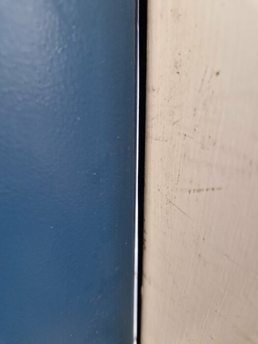 Närbild av en blå yta bredvid en smutsig vit vägg, med kontrasterande färger och texturer.