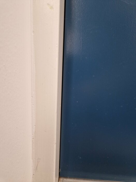 En vit dörrkarm och en del av en blå dörr med textur och synliga bruksspår.