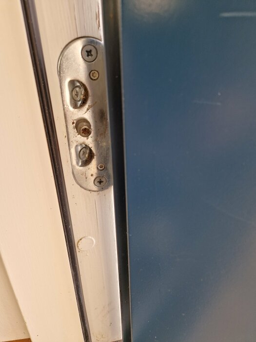 Förslitna skruvar på en dörrlås-stolpe, nära kant, vit dörrkarm och blå dörr.