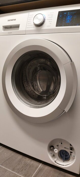 Siemens tvättmaskin, frontlastare, digital display, vred, programval, öppen avloppspumpslucka i förgrunden.