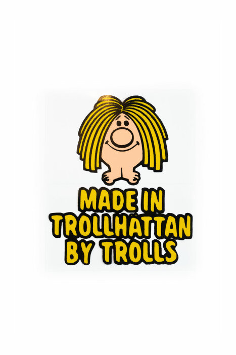 Tecknad figur, långhårig, stort leende. Text: "Made in Trollhättan by Trolls". Gul, svart och vit färgsättning.