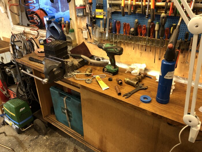Verkstadsbord med verktyg, oordning, skruvstycken, elverktyg och diverse föremål i arbetsmiljö.