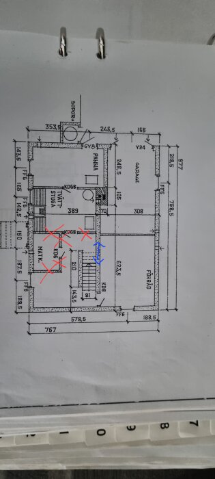 Arkitektonisk ritning av en byggnadsplan med mått och rumsmarkeringar, upphängd i en pärm, anteckningar med rött.