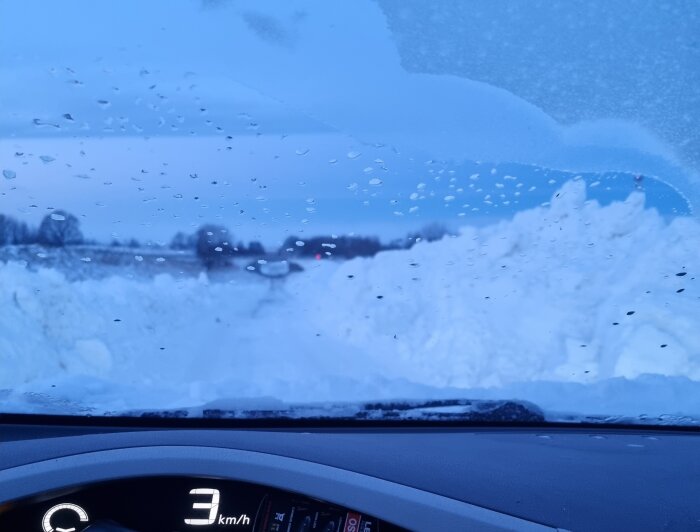 Vy från bil, snöig väg, droppar på vindruta, hastighetsmätare visar 3 km/h.