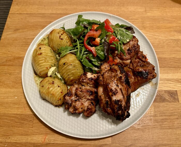 En tallrik med grillad kyckling, hasselbackspotatis och färsk sallad. Smakfull hemlagad måltid.