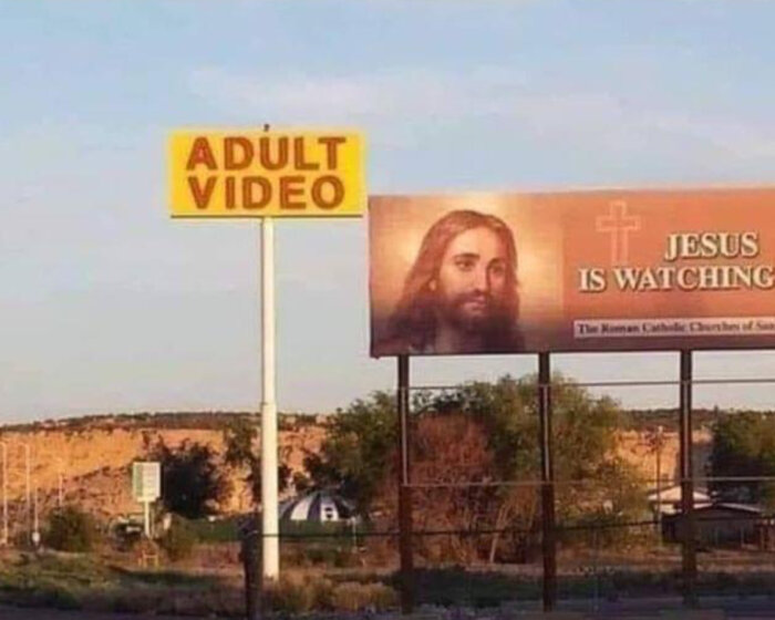 Skylt för vuxenvideo bredvid stor reklam med Jesus och texten "Jesus is watching". Kontrasterande budskap.