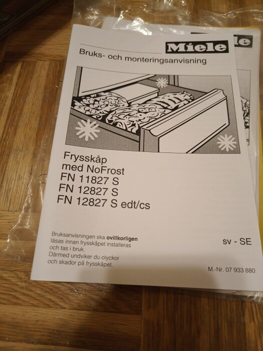 Användarmanual för Miele NoFrost frysskåp, produktmodeller FN 11827 S och FN 12827 S, varningsinstruktioner, trägolv i bakgrunden.