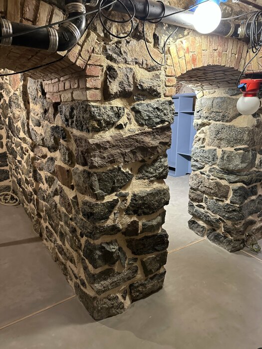 Rustik källare med stenväggar, tegelbågar och modern belysning.