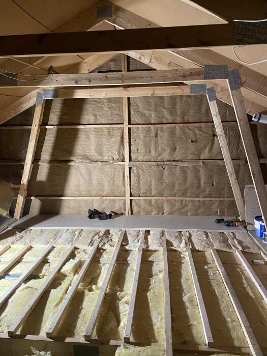 Vindsvåning under konstruktion med isolering, träsparrar, verktyg och inbyggnadsklara strukturer.