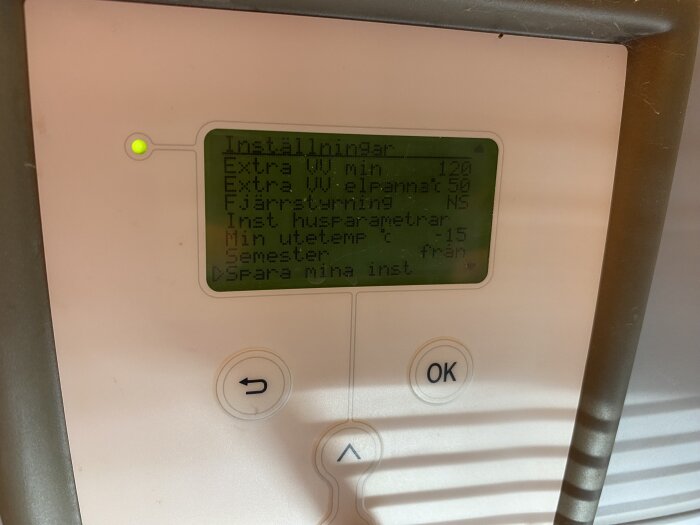 Digital termostat visar menyalternativ för värmeinställningar och temperaturer på svenska, omringad av panel och rör.
