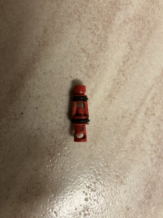 Röd LEGO-figur utan armar och huvud på en marmorerad, ljusbrun yta.