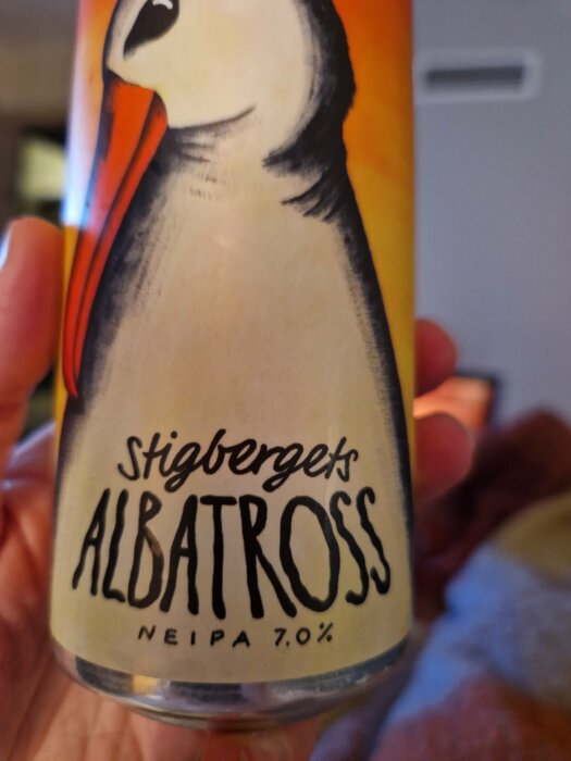 Burk med albatross, "Stigbergets Albatross NEIPA 7.0%", hand håller, delvis oskarp bakgrund.