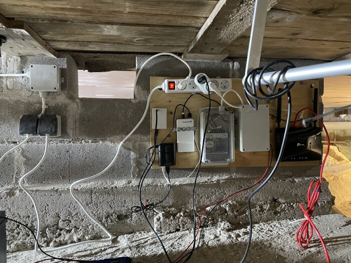 Elektrisk utrustning och kablar monterade oorganiserat på en vägg under ett träbjälklag.