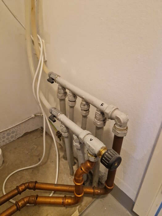 Vattenrör och ventiler oorganiserat installerade mot en vägg, blandade material och färger, renoveringsprojekt.