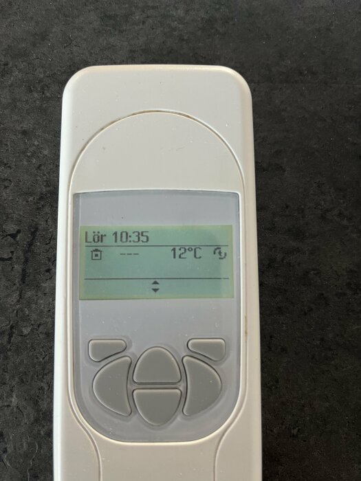 Digital termostat visar tid och temperatur på en LCD-skärm, placerad på en mörk yta.