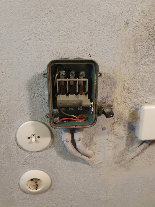 Öppen elektrisk kopplingslåda på vägg med uttag och strömbrytare.