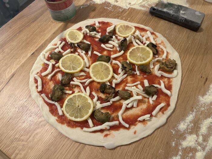 Opreparad pizza med tomatsås, ost, citronskivor och gröna grönsaker. Bakbord med mjöl och kakform.