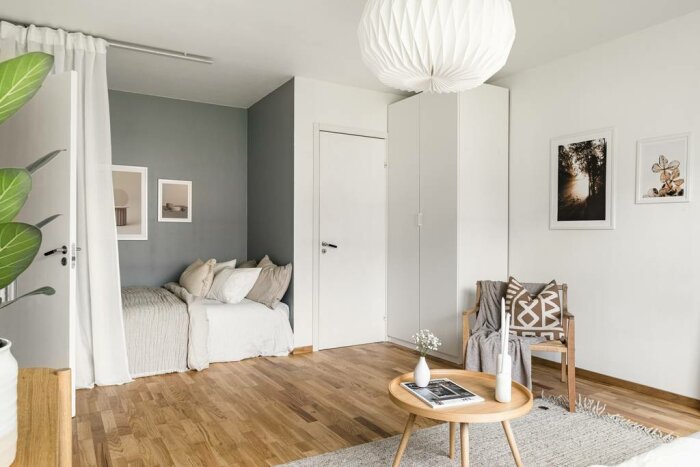 Modernt sovrum, minimalistisk stil, neutrala färger, trägolv, konstvägg, stor växt, hängande lampa.