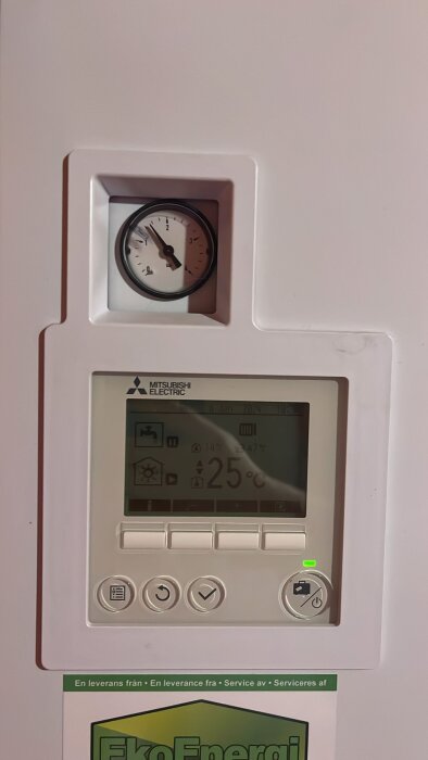 Analog klocka och Mitsubishi Electric termostat med temperaturdisplay på en vägg, tillhörande Eko Energi.