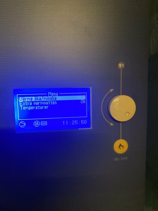 Digital kontrollpanel för värmesystem med blå bakgrundsbelysning, gul ON/OFF-knapp, svensk text och klocka.