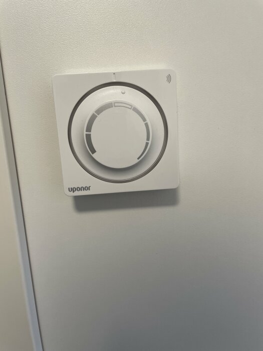 Vit termostat på vägg, märkt "Uponor", med vred och Wi-Fi-symbol.