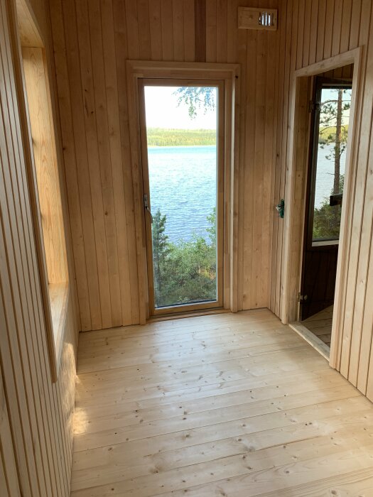 Ett tomt trärum med dörr som visar utsikten över en sjö.