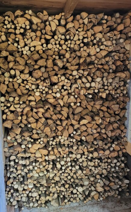 Stapelade vedträn i vedbod, varierande storlek och form, torra, redo för förbränning.