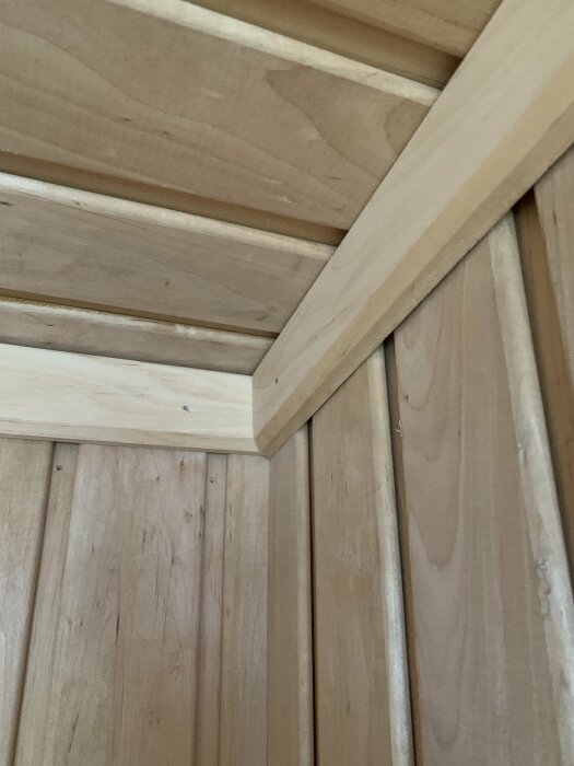 Träpanel och lister i interiör, tak och vägg möts. Naturmaterial, grovt finishat, enkel design.