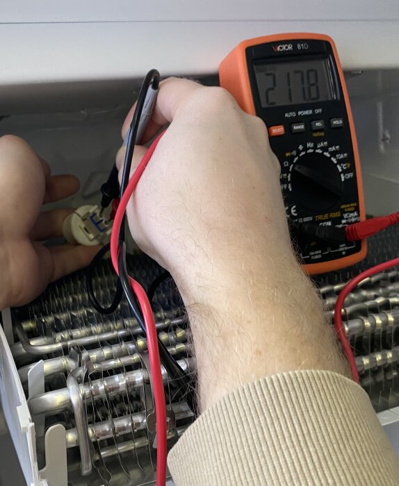 Person mäter spänning med multimeter på elektronisk apparat.