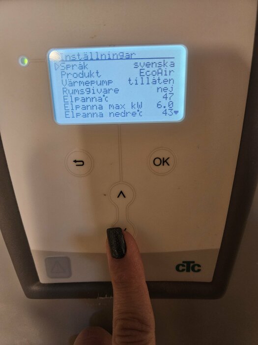 En hand trycker på en knapp på en termostat med en svensk meny. Inställningar för värmepump visas.