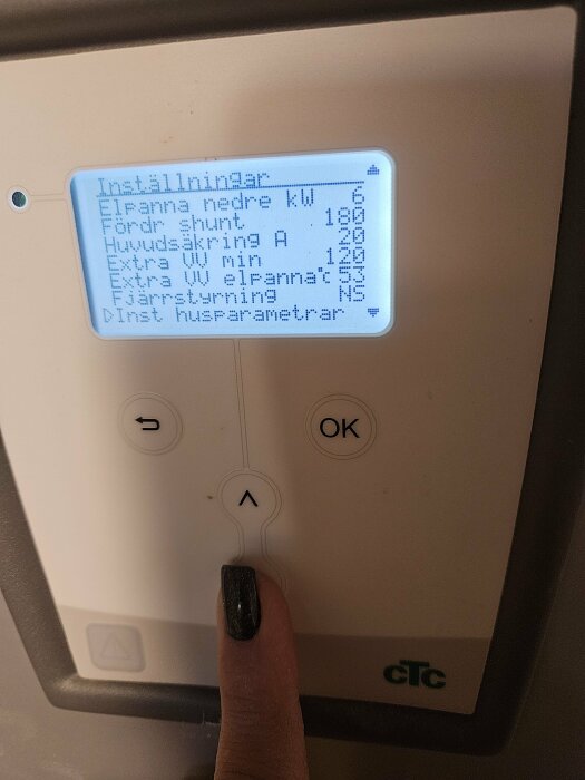 Digital display på en värmepump eller termostat med menyval; finger trycker på en knapp.