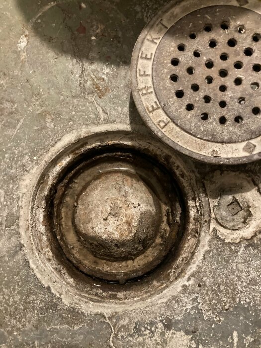 Bild på en öppen golvbrunn med bortlyft galler, smutsiga och slitna betongytor synliga.