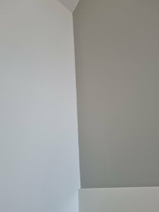 Hörn av ett rum med vita och grå väggar och skuggspel. Enkel, minimalistisk, modern inredning.