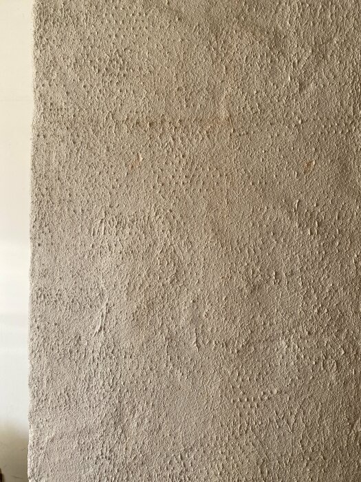 Vägg med grov, strukturerad beige puts. Ljusspel skapar skuggor och höjder.