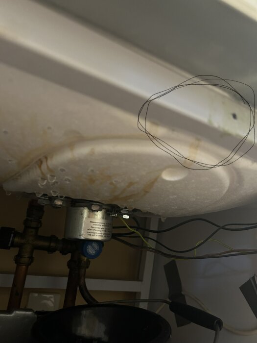 En bild under en diskbänk med rör, isolering, vattenläckage och mögelskador markerade med en cirkel.