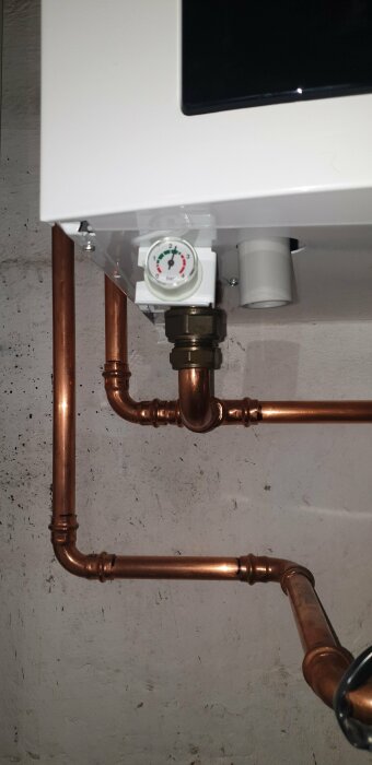 Värmesystem, kopparledningar, manometer, vitt kabinett, betongvägg, installation.